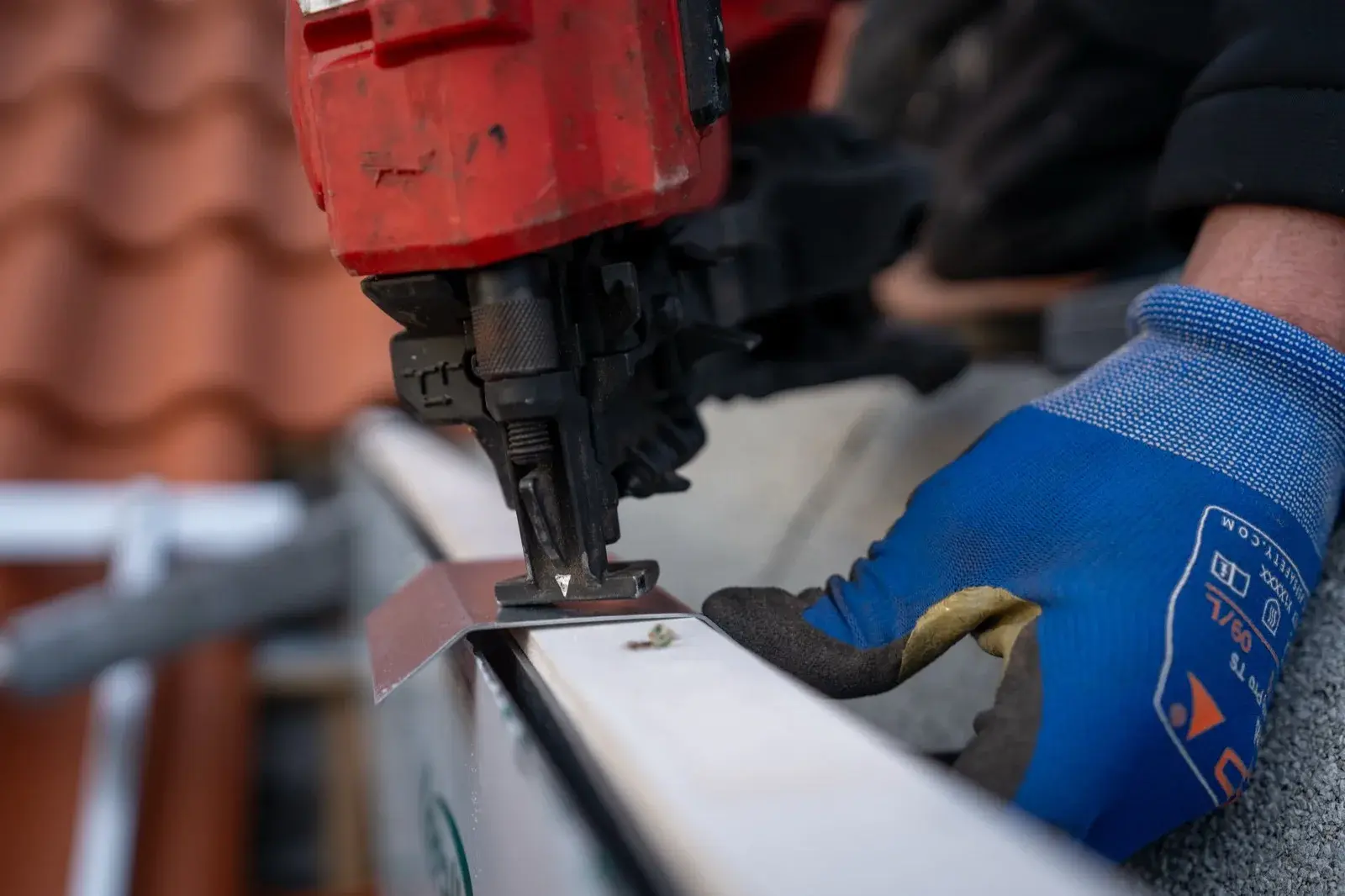 Close-up van een hand met werkhandschoen die een metalen gootrand vastschiet langs een pannendak