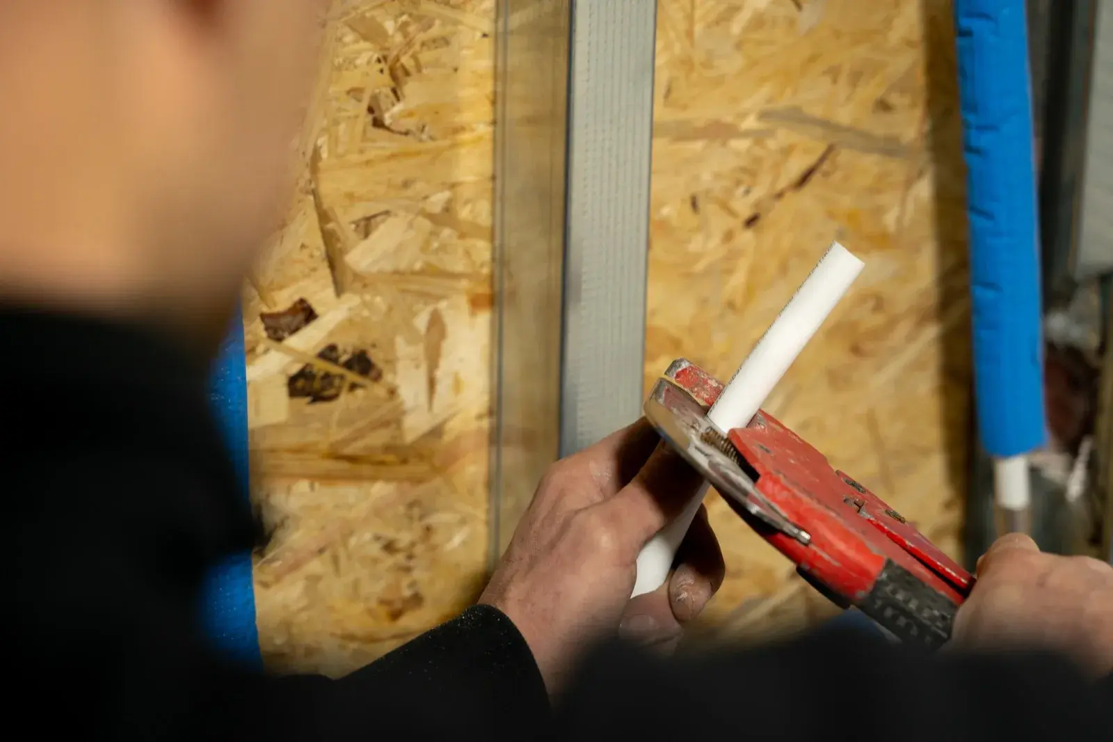 Loodgieter knipt met een buizensnijder een kunststof waterleiding op maat bij een wand in aanbouw